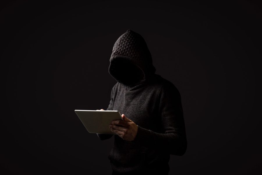 Faceless man in a hoodie with a hood holds a tablet in his hands