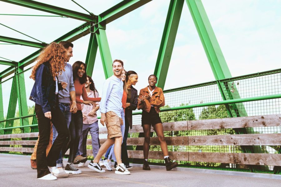 a group of multiracial young people walking together crossing a bridge on a beautiful weekend day - lifestyle concept of friendship, brotherhood between different cultures, racial integration and internationalization